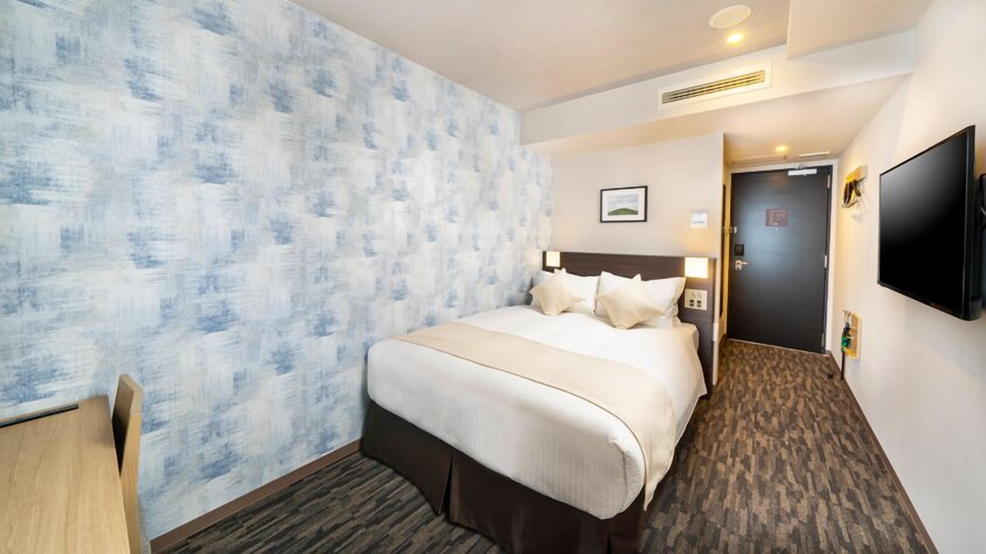 Quarto de hotel com uma cama grande, uma escrivaninha, uma TV e uma porta que dá para outro quarto.