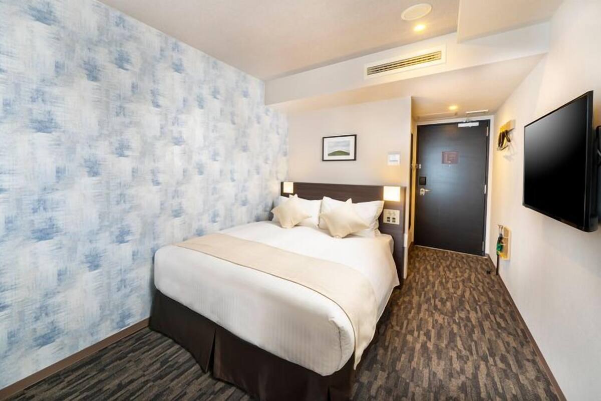 A hotel room with a large bed, a desk, a TV, and a door leading to another room.