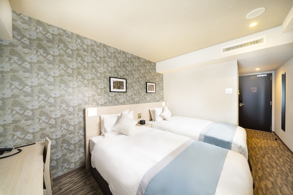 A hotel room with two beds, a desk, and a patterned wallpaper.