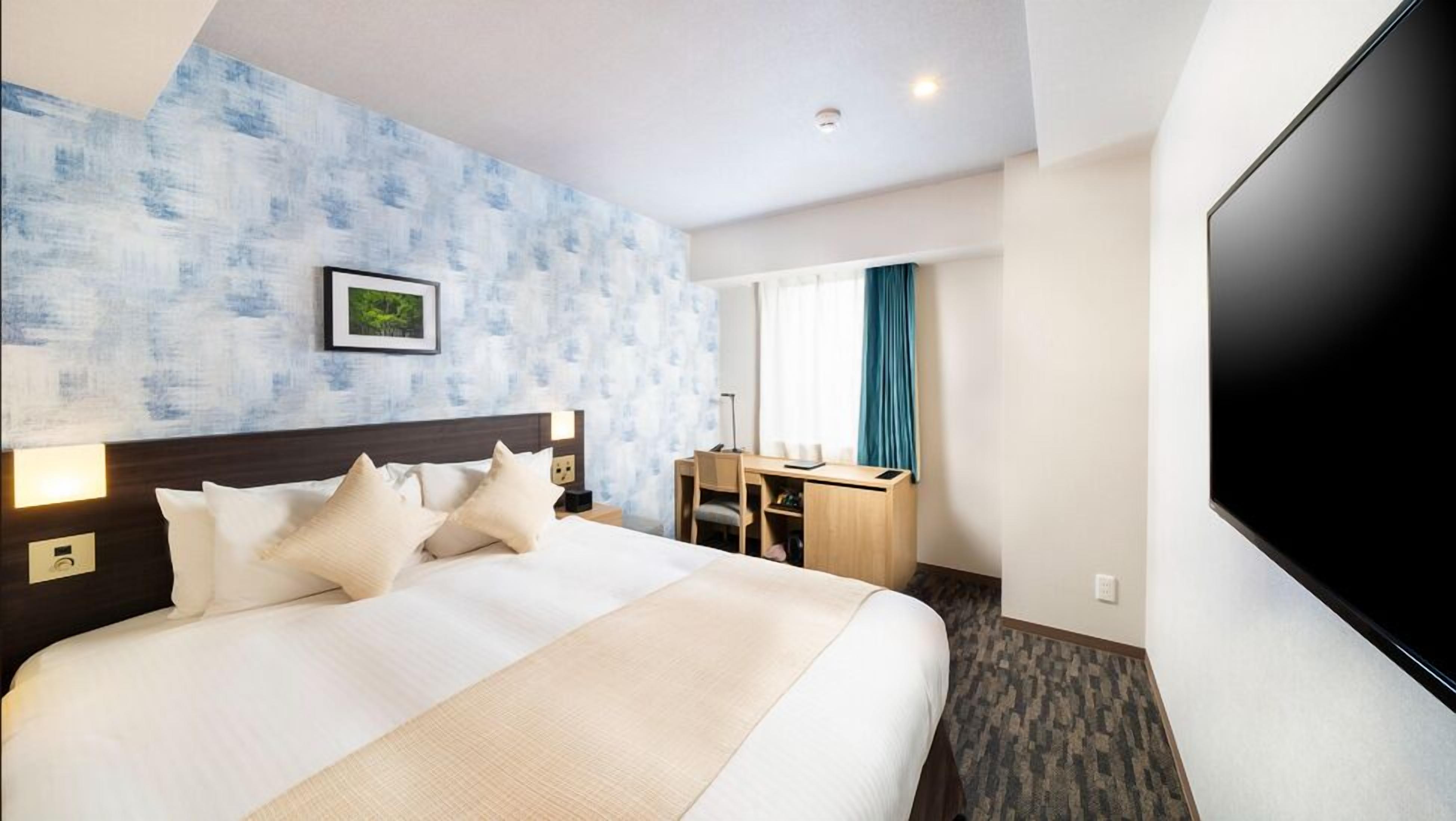 Quarto de hotel com cama, escrivaninha e televisão.