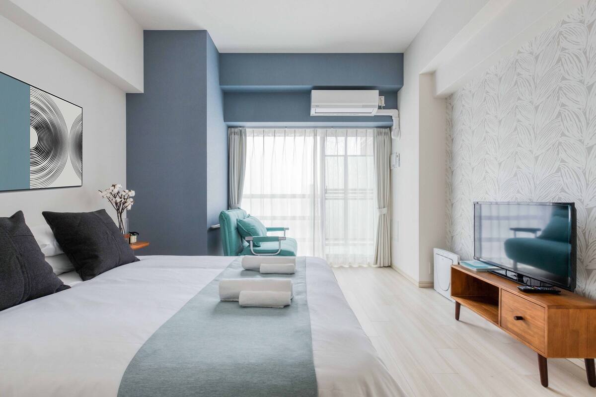 Ein modernes Hotelzimmer mit einem großen Bett, einem Fernseher und einer Sitzecke mit Stuhl und Tisch.