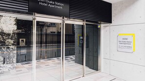 The exterior of the Shin-Osaka Station Hotel Apartment with a modern design, including a glass entrance and a signboard.