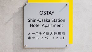 A sign for the OSTAY Shin-Osaka Station Hotel Apartment with Japanese text.