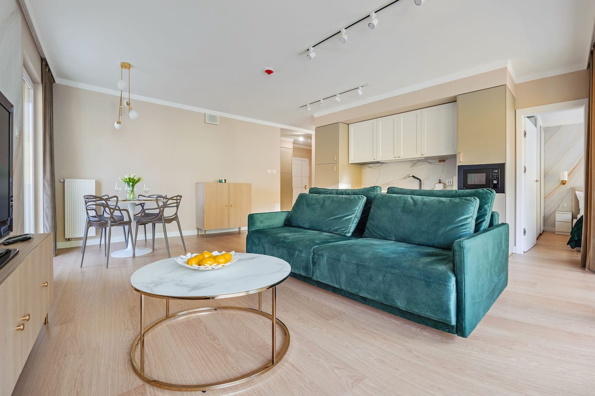 A modern living room with a green sofa, a marble coffee table, and a dining area with chairs and a table.