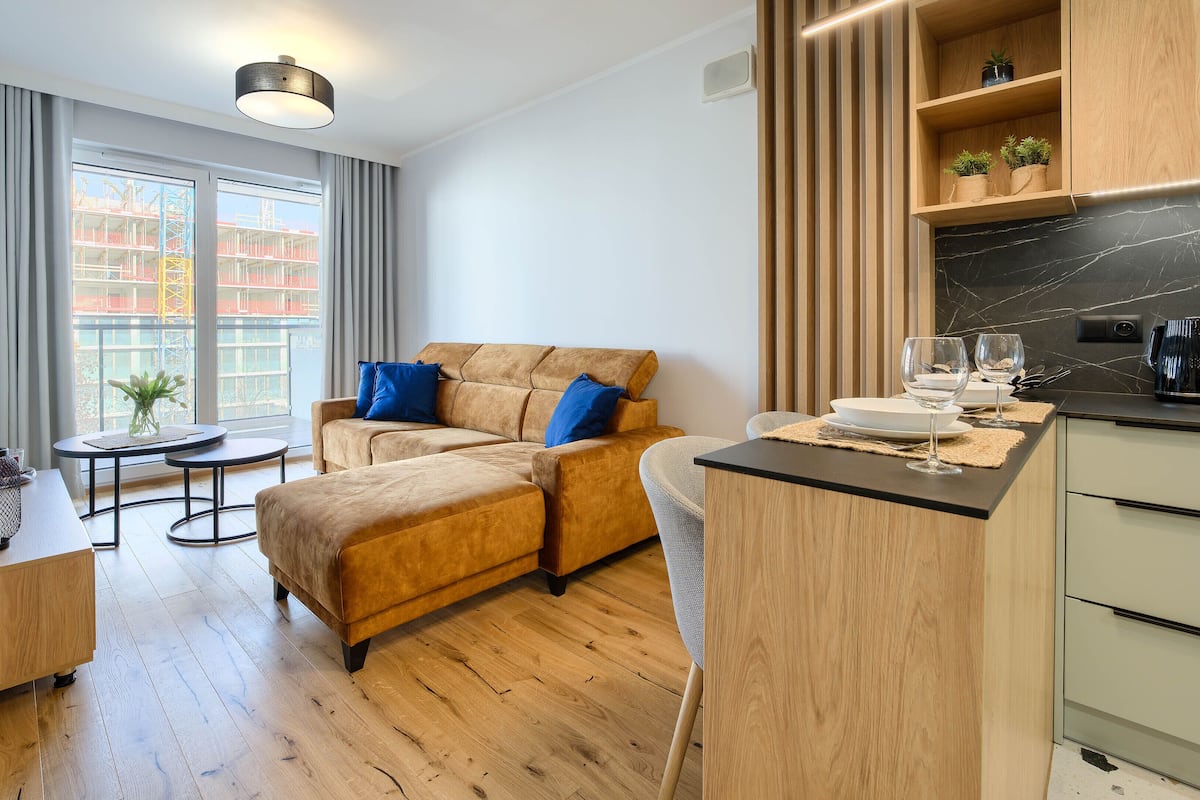 A modern living room with a sofa, a dining table, and a kitchen area with wooden cabinets and a marble countertop.