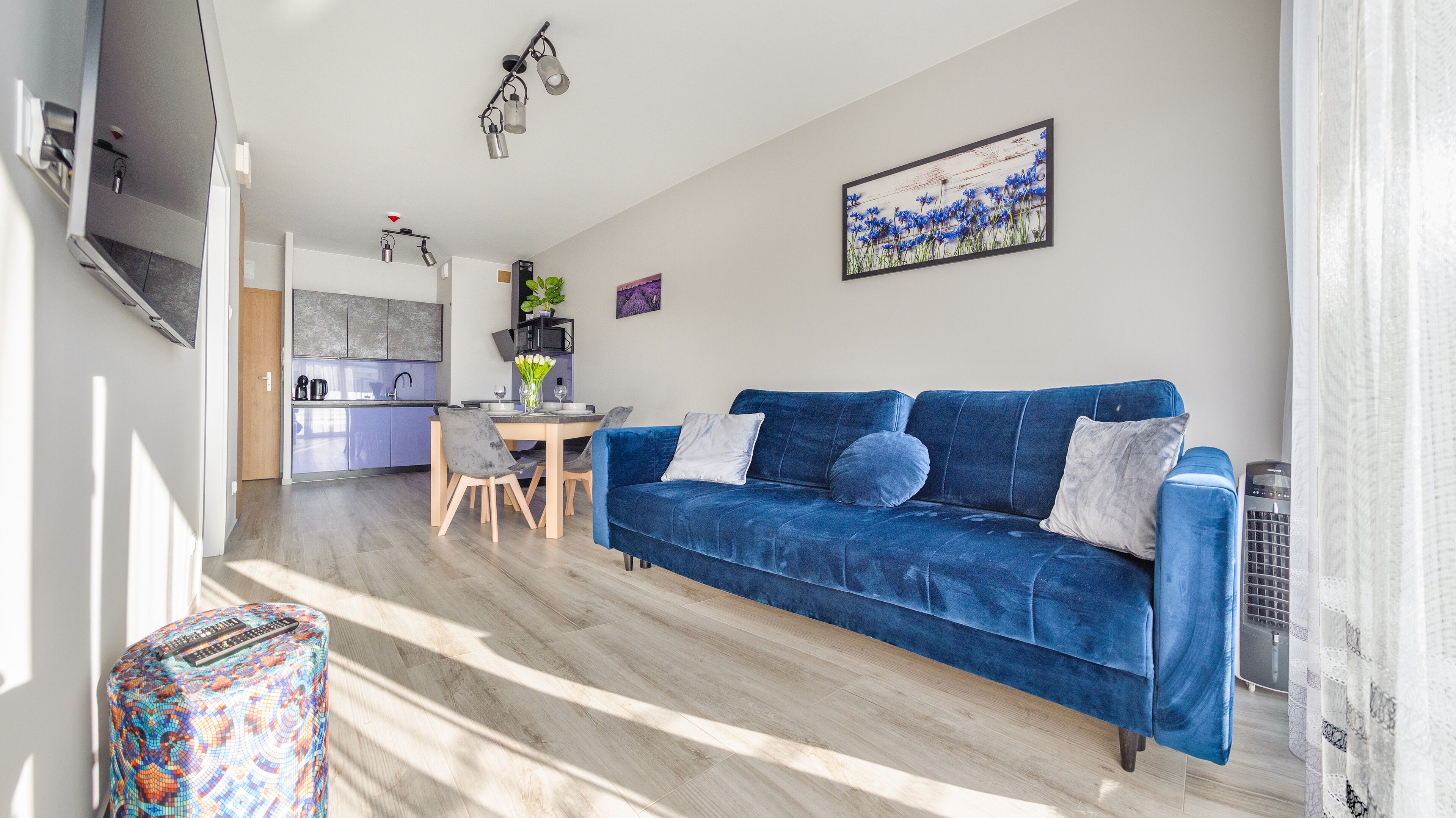 A modern living room with a blue sofa, a dining table, and a kitchen in the background.