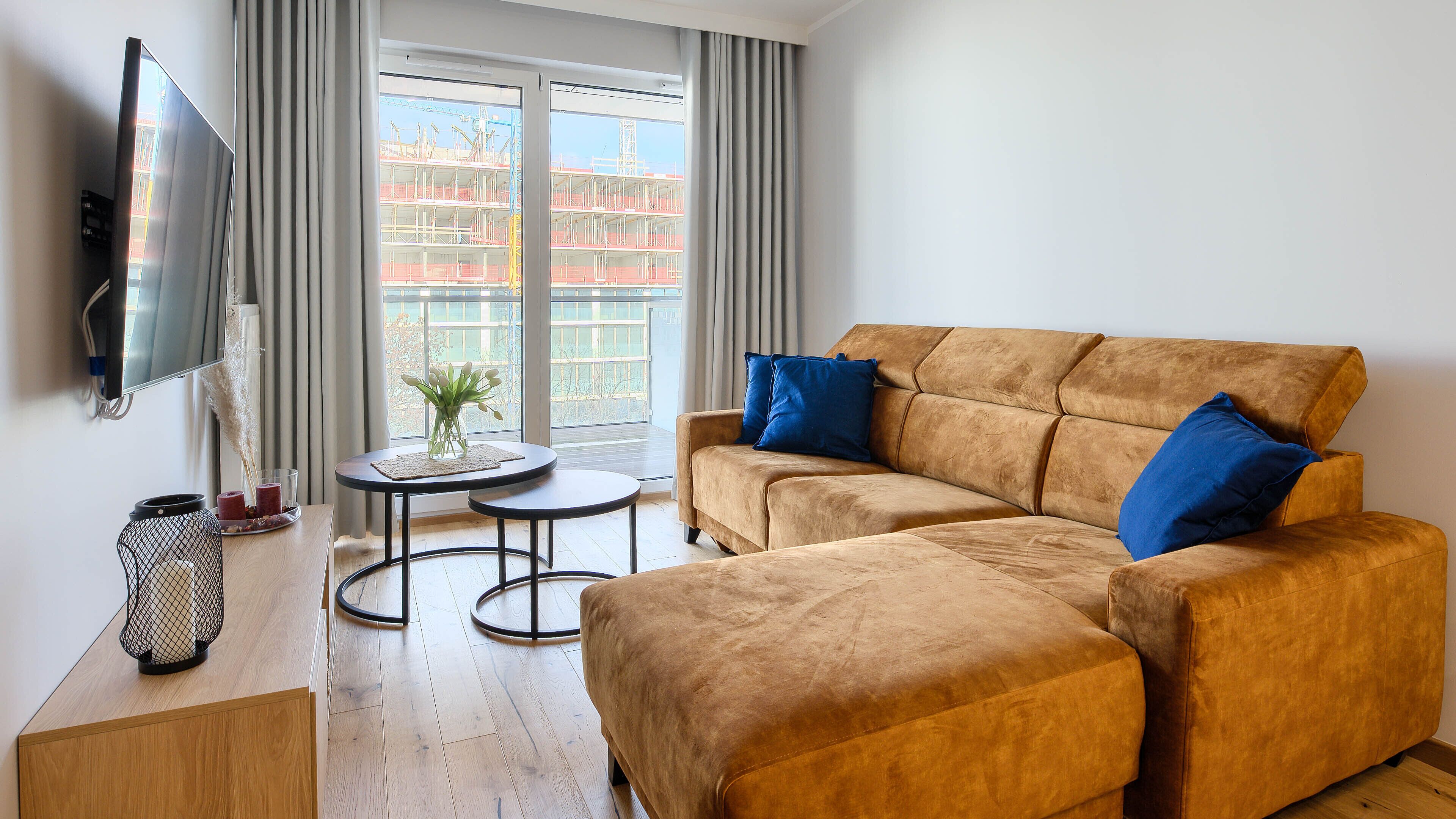 A living room with a sofa, two side tables, a TV, and a window with a view of a building.