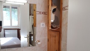 Une salle de bain avec un lavabo blanc, un miroir, une porte en bois et une fenêtre avec des rideaux.