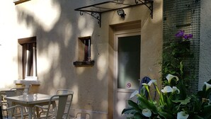 Une terrasse avec une table et des chaises, une porte et une petite fenêtre.
