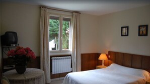 Une chambre d’hôtel avec un lit, une petite table sur laquelle est posé un vase de fleurs, une lampe, un radiateur et un téléviseur sur un meuble.