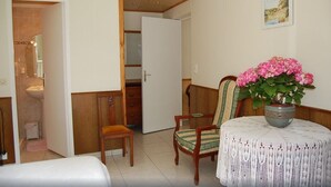 Une pièce comprenant un lit, une chaise, une table ornée d’un vase de fleurs et une porte donnant sur une salle de bain.