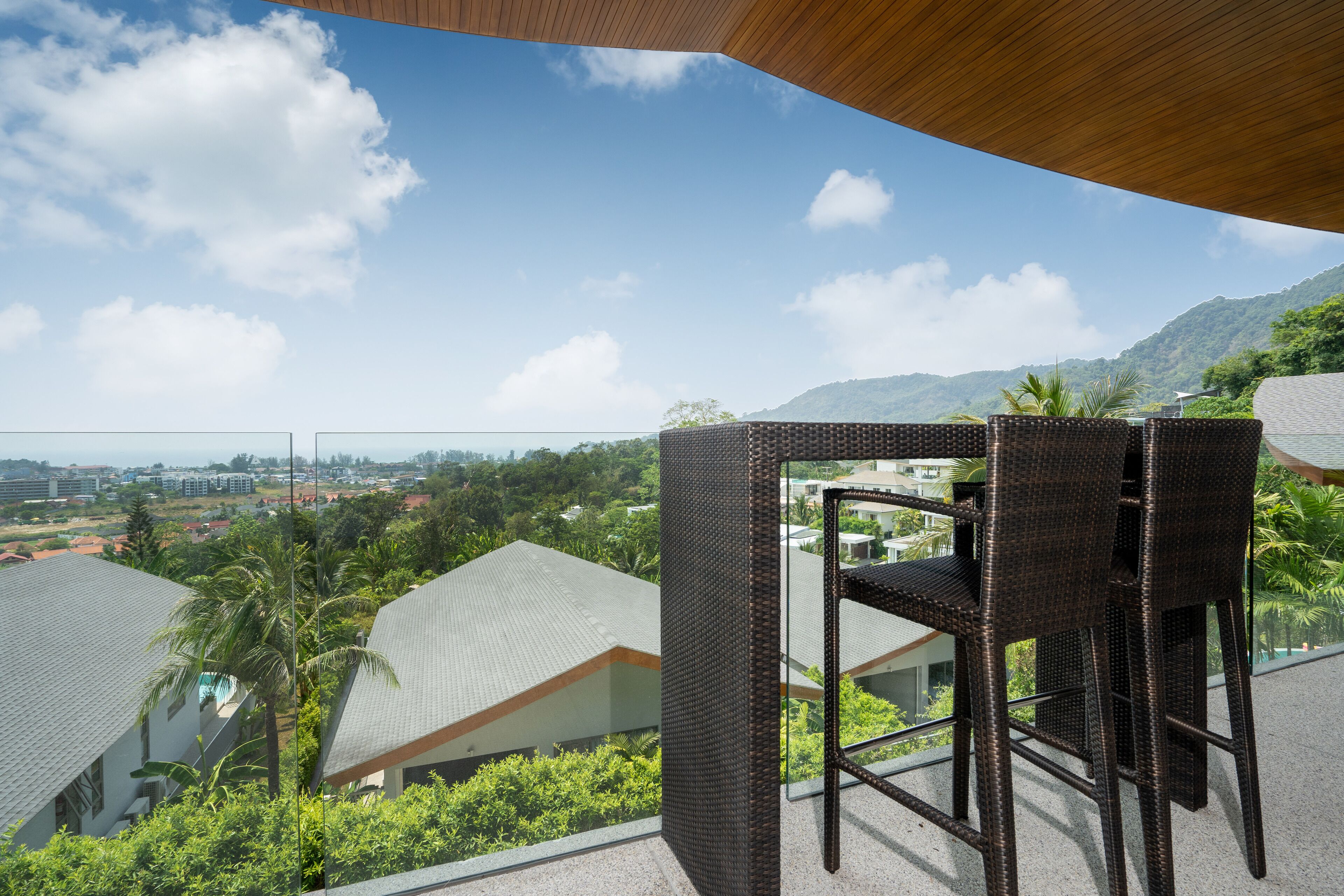 A balcony with wicker furniture overlooking a residential area with houses and palm trees.