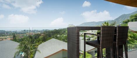 A balcony with wicker furniture overlooking a residential area with houses and palm trees.