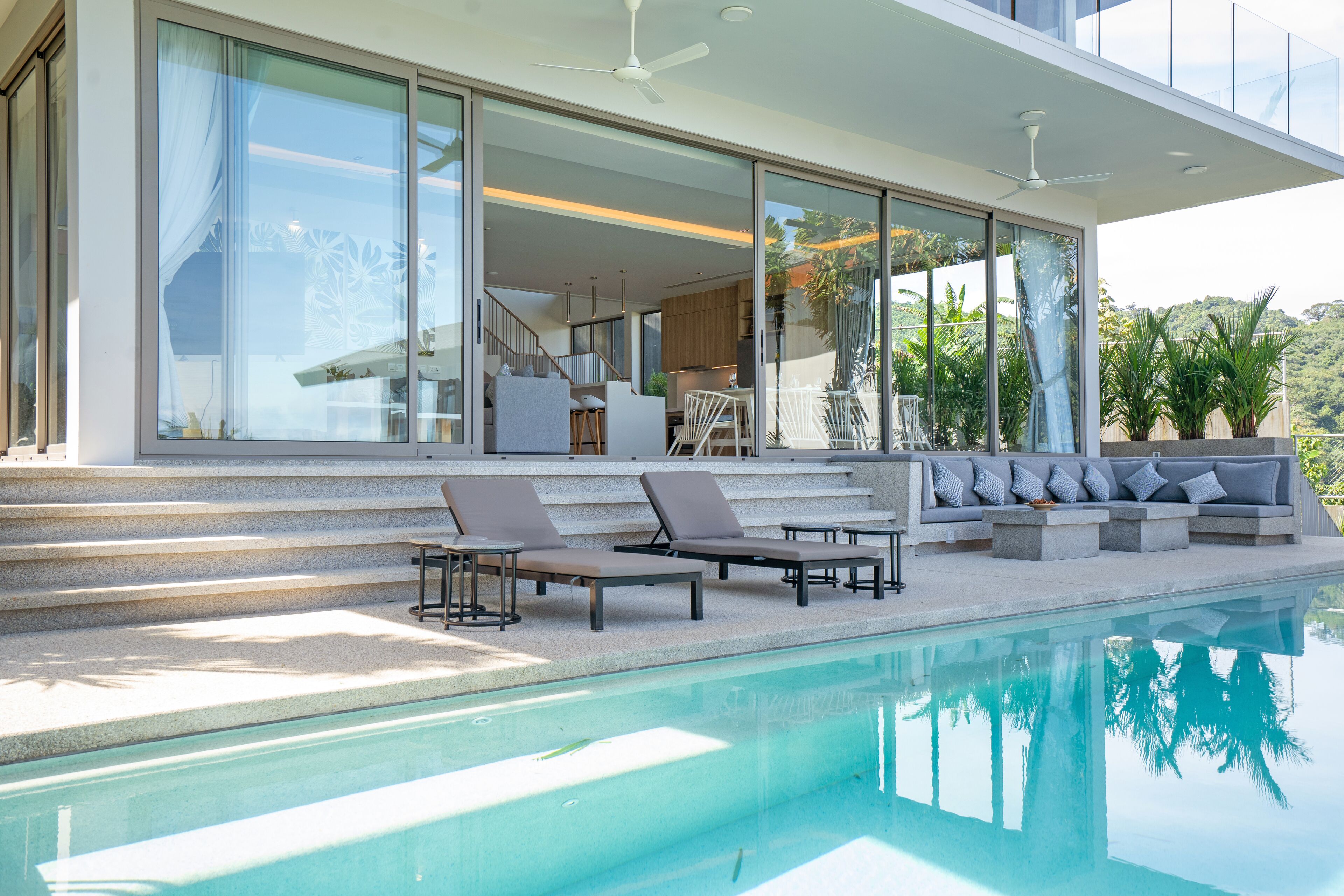 A modern house with a swimming pool, outdoor seating, and large glass windows.