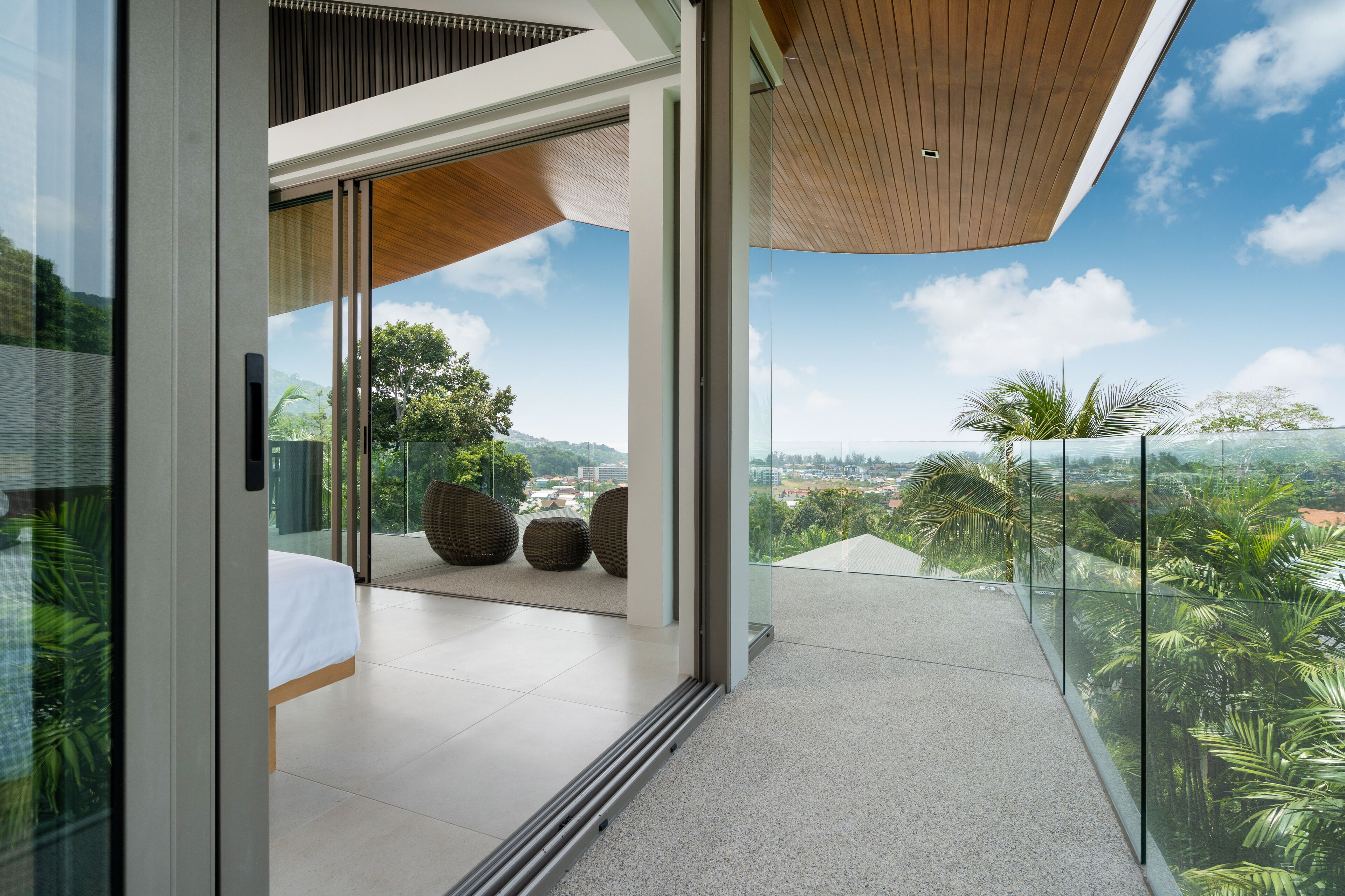 A modern hotel room with a balcony, large windows, and a view of the city and greenery.
