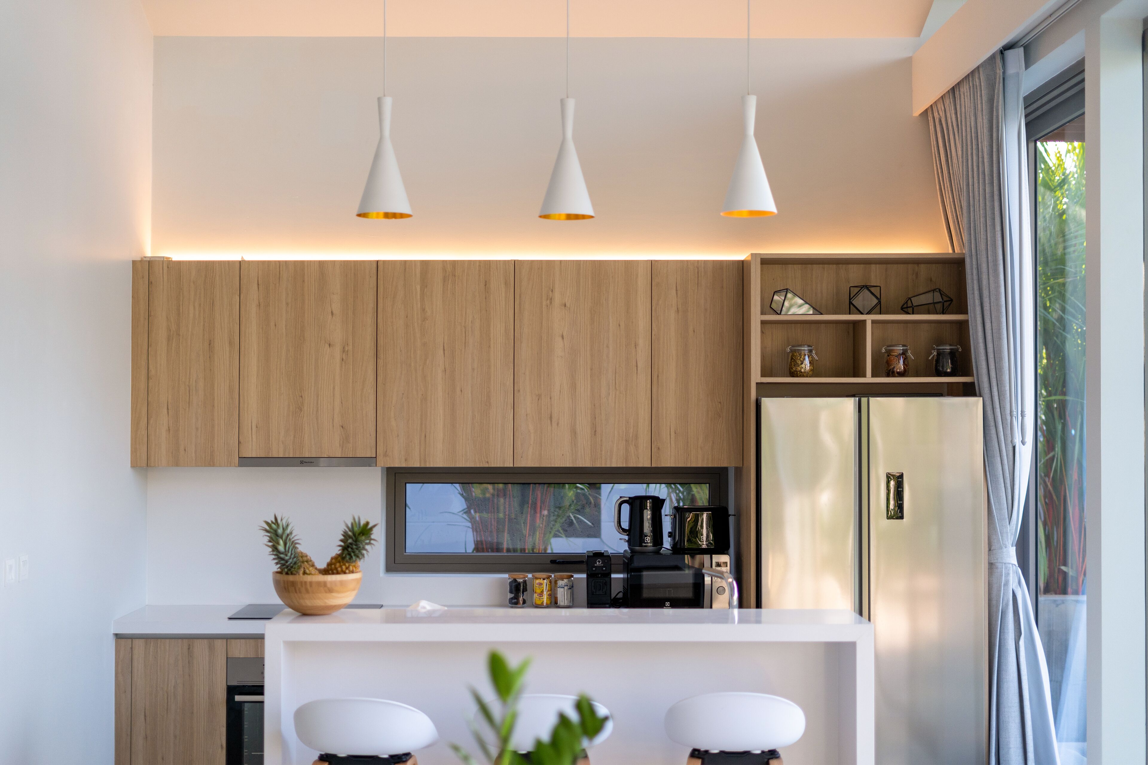 Une cuisine moderne avec des meubles en bois, un plan de travail blanc, une machine à café intégrée et un réfrigérateur.