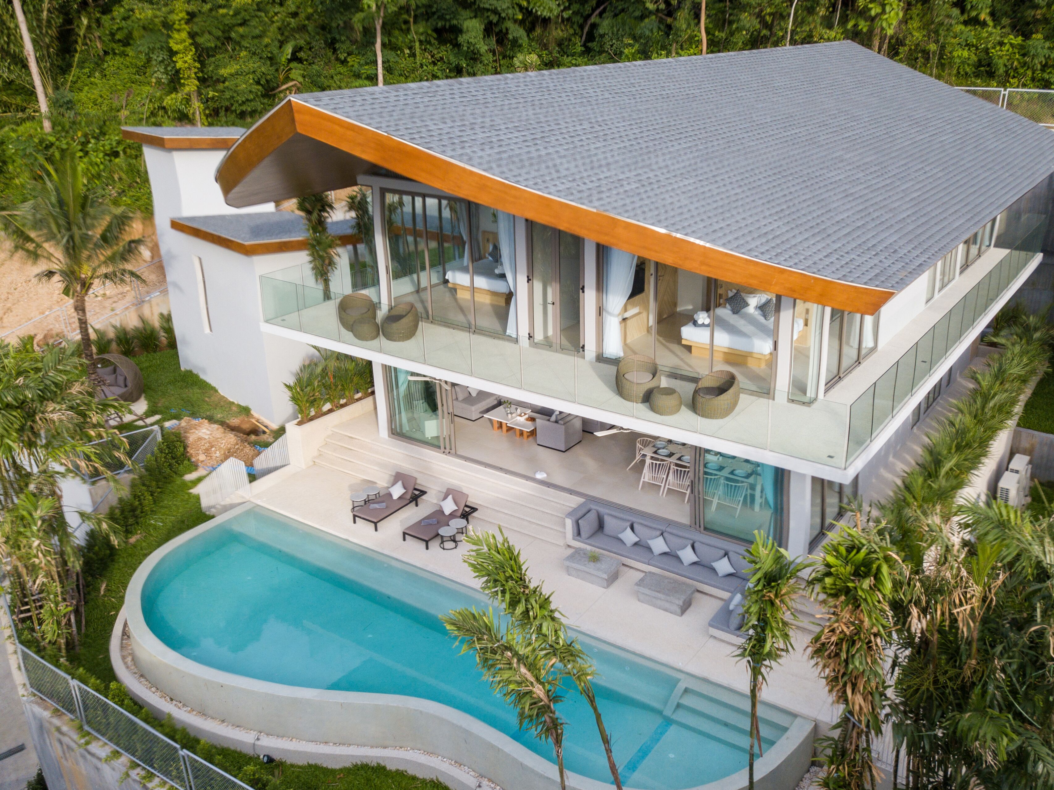A modern two-story house with a swimming pool, outdoor seating, and lush greenery.