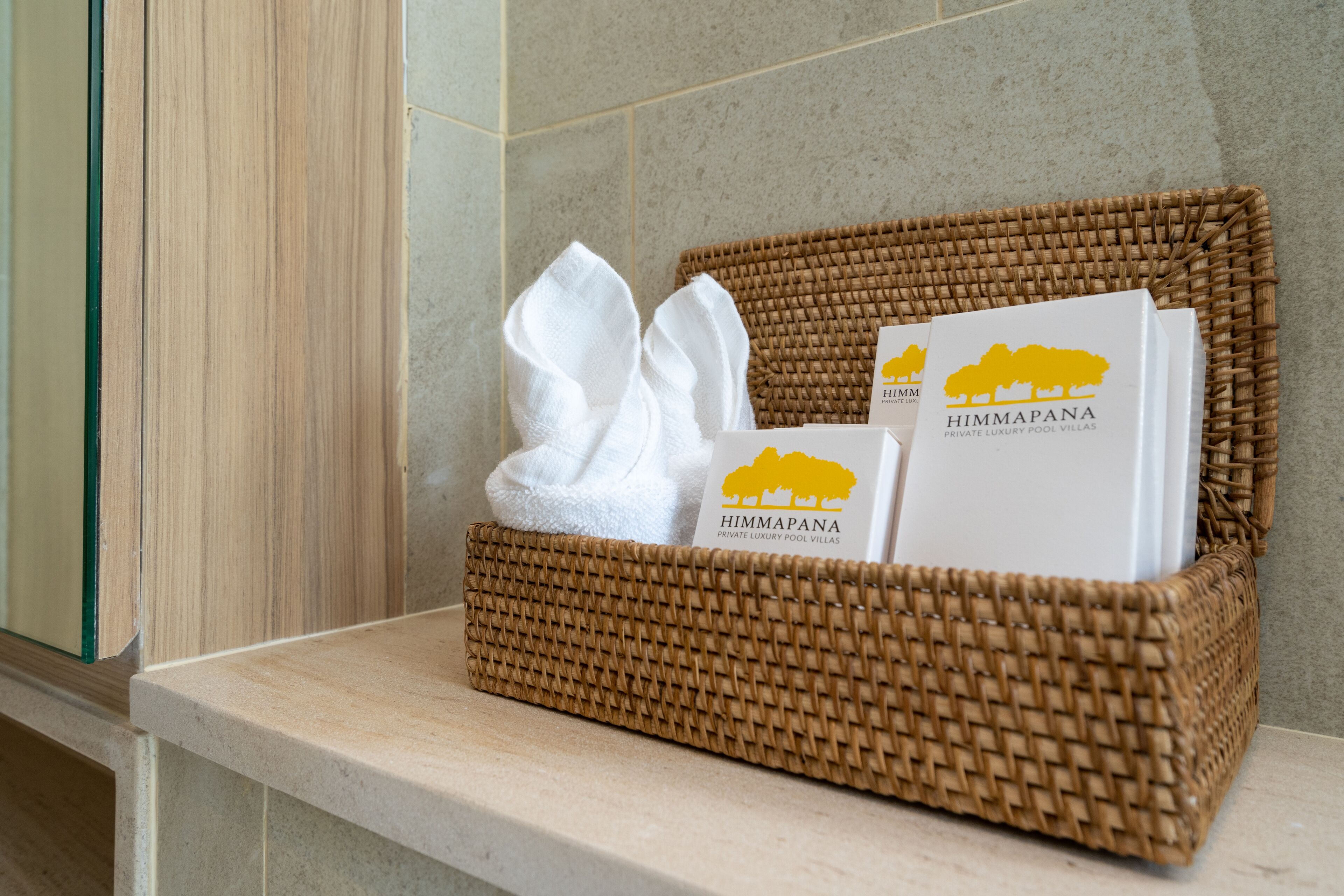 A wicker basket containing a white towel and two brochures for 'HIMMAPANA PRIVATE LUXURY POOL VILLAS'.