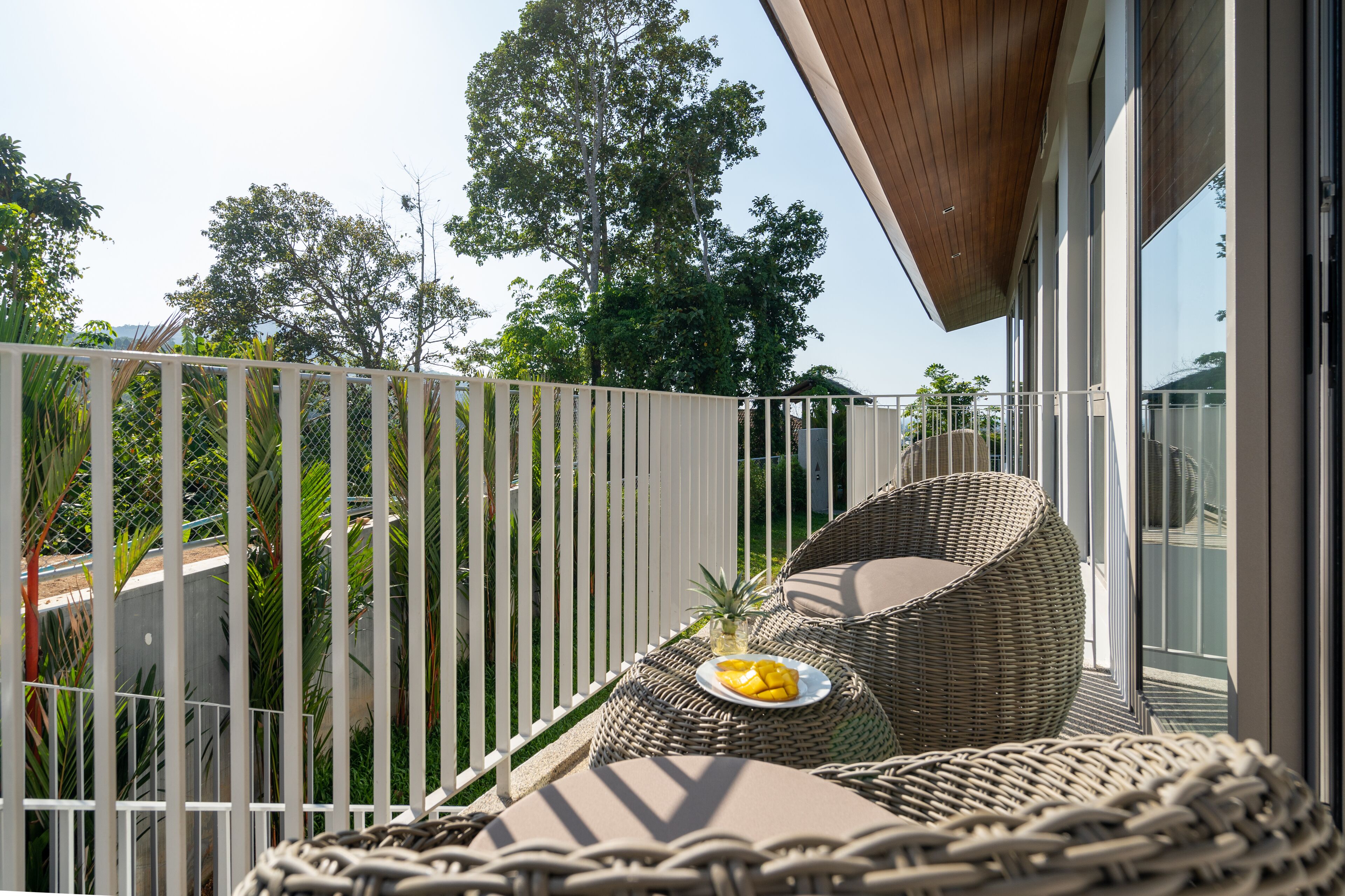 A balcony with wicker furniture, a plate of fruit, and a view of trees and buildings.