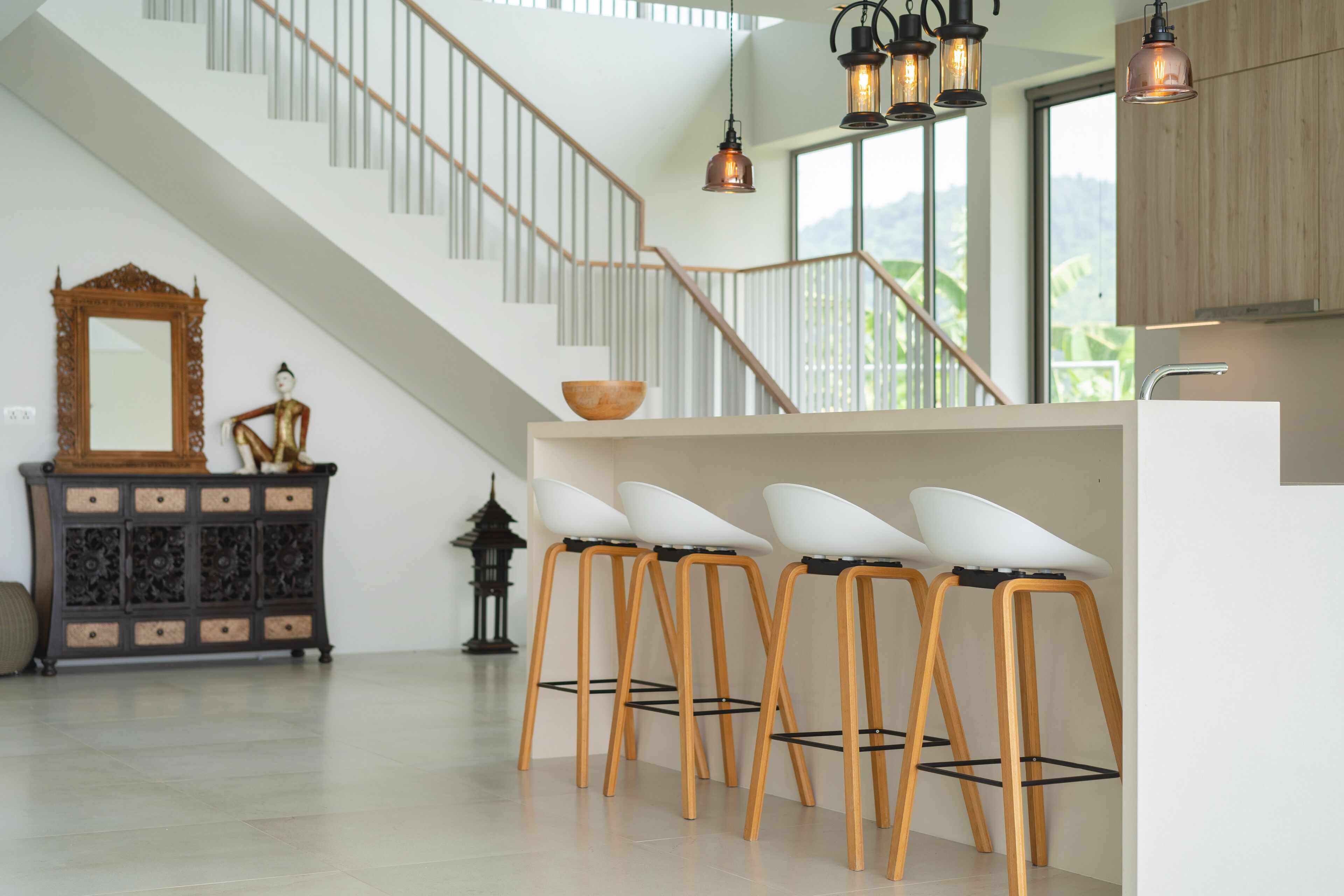 Una cocina moderna con una isla central, taburetes de madera y una escalera con barandilla.
