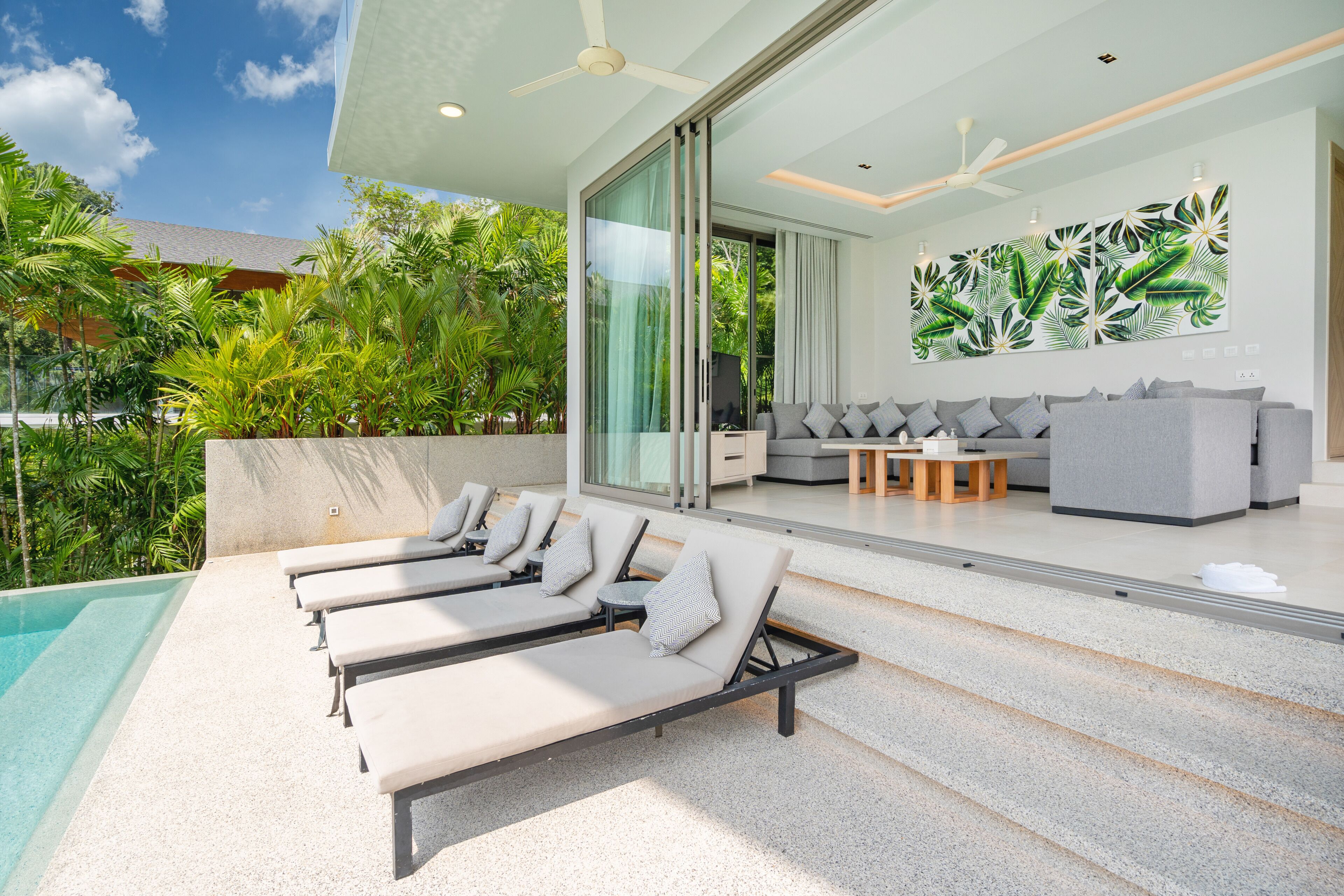 A modern outdoor lounge area with sun loungers, a pool, and a seating area with a sofa and coffee table.