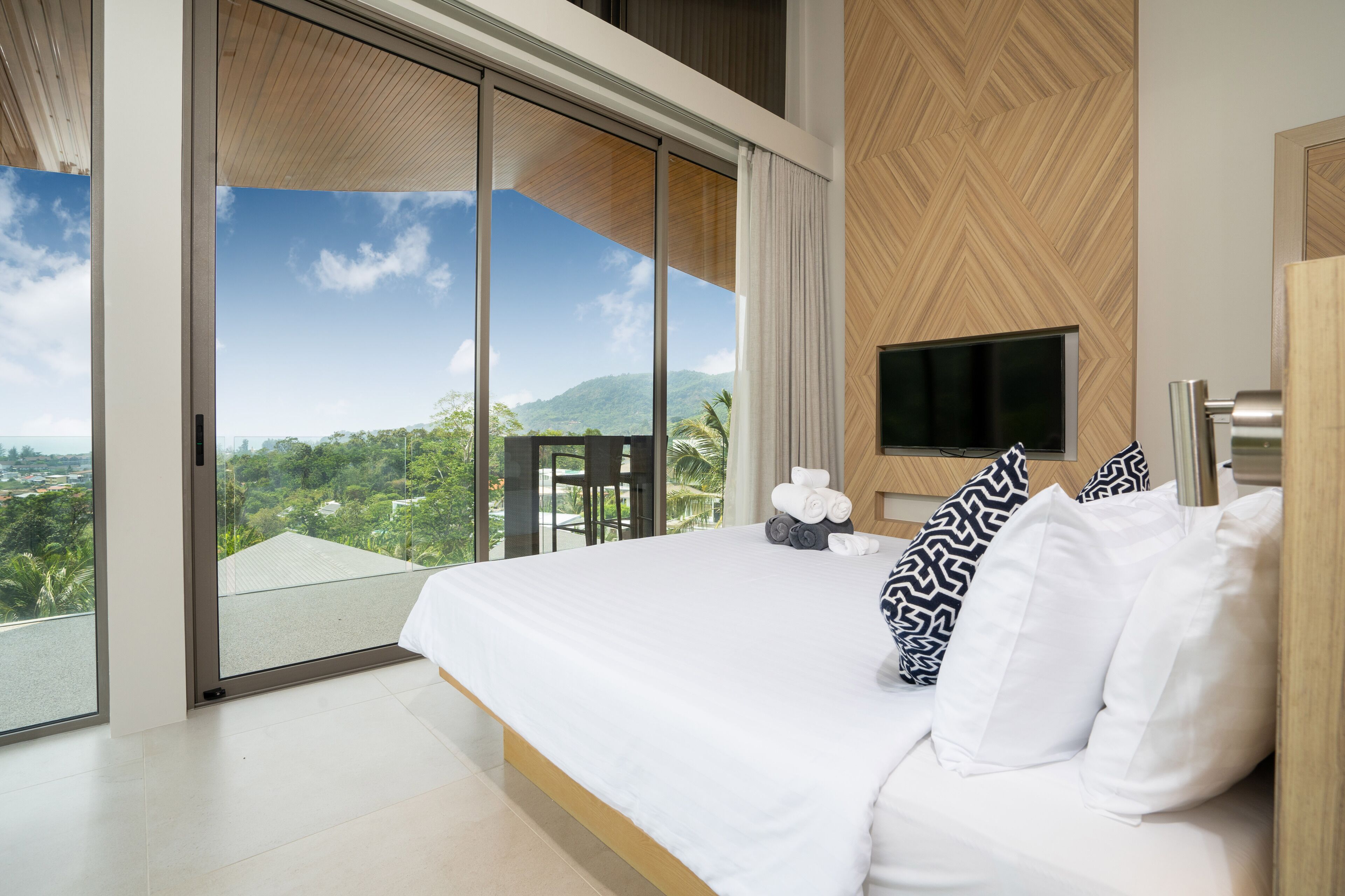 A modern hotel room with a large bed, a flat-screen TV, and a balcony with a scenic mountain view.