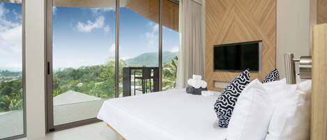 A modern hotel room with a large bed, a flat-screen TV, and a balcony with a scenic mountain view.