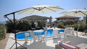 Et poolområde med pool, hvide stole, parasoller og en pergola.