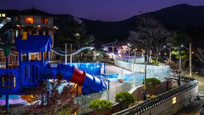 A resort with a pool area, a blue and red slide, and a building with a lit entrance.