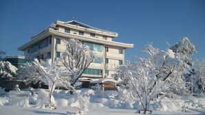 A multi-story building with a traditional architectural style, surrounded by snow-covered trees and a clear blue sky.