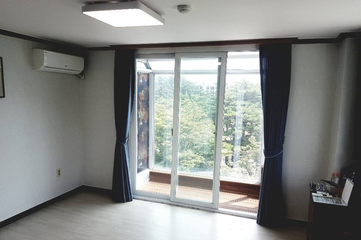 Ein Zimmer mit einer großen Schiebeglas-Tür, die auf einen Balkon führt, einer Decken-Klimaanlage und einem Holzboden.