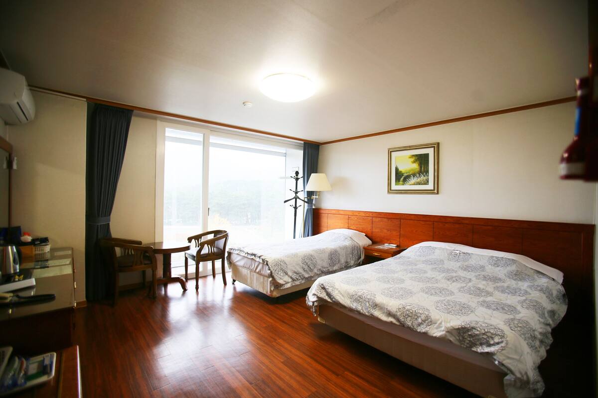 Ein Hotelzimmer mit zwei Betten, einem Schreibtisch, einem Stuhl und einem Fenster mit Vorhängen.