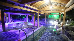 A spa area with a stone pool, wooden deck, and seating area under a wooden roof structure.