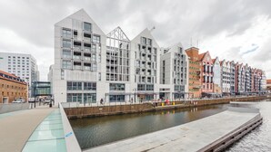 A waterfront hotel with modern architecture, a riverside promenade, and a pedestrian bridge.