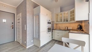 A modern kitchen with white cabinetry, a built-in oven, a coffee machine, and a dining area with a white table and chair.
