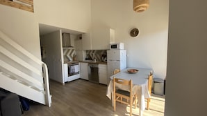 Cozinha compacta com eletrodomésticos brancos, mesa de jantar com cadeiras e escada que leva a outro cômodo.