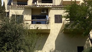 Edifício com vários andares, varandas, aparelhos de ar condicionado e área de jardim com gramíneas altas.