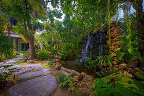 Un jardin luxuriant avec une cascade, des marches en pierre et un feuillage dense.