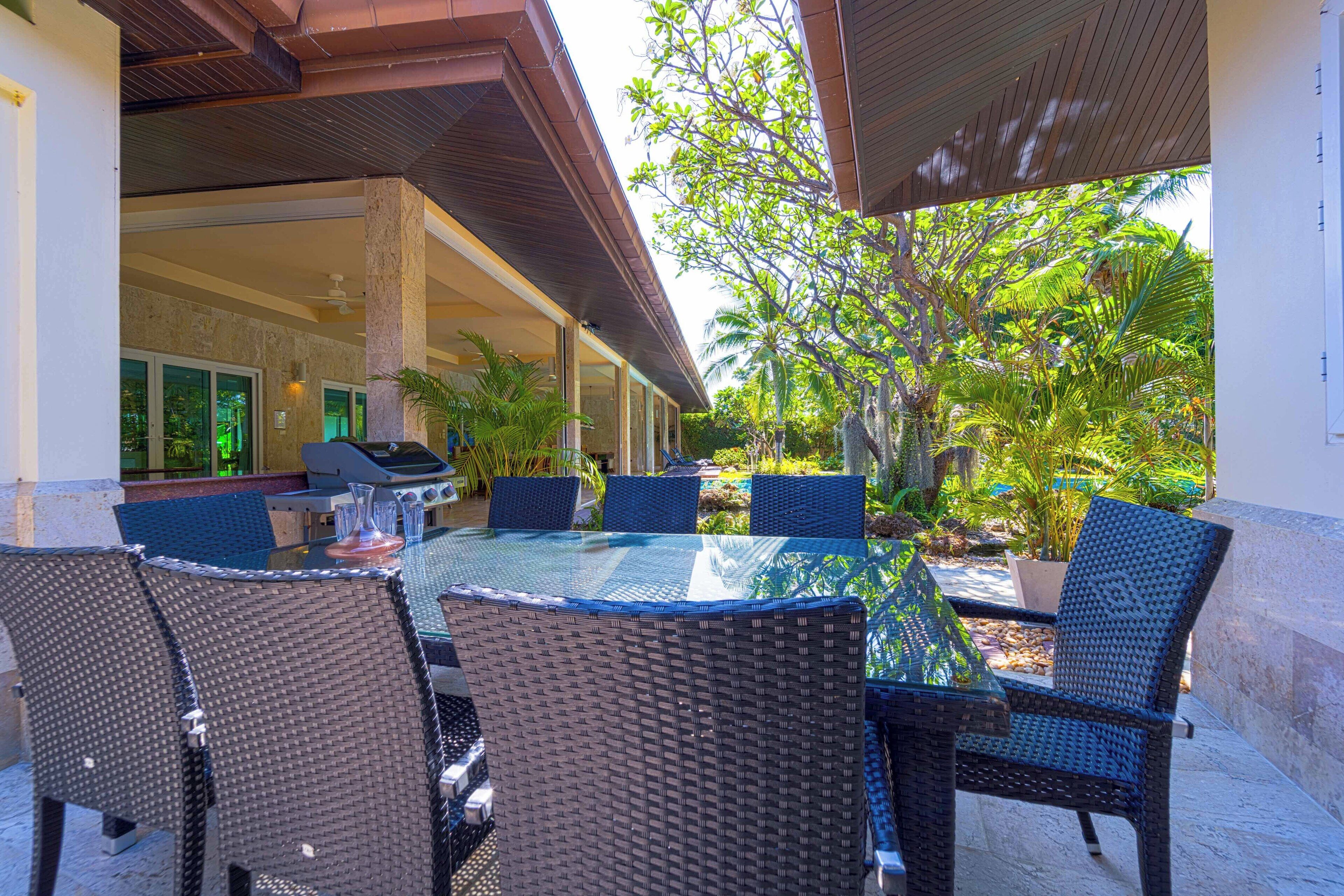 Une terrasse extérieure avec une table ronde en verre, entourée de chaises en osier, un barbecue et des plantes en pot.