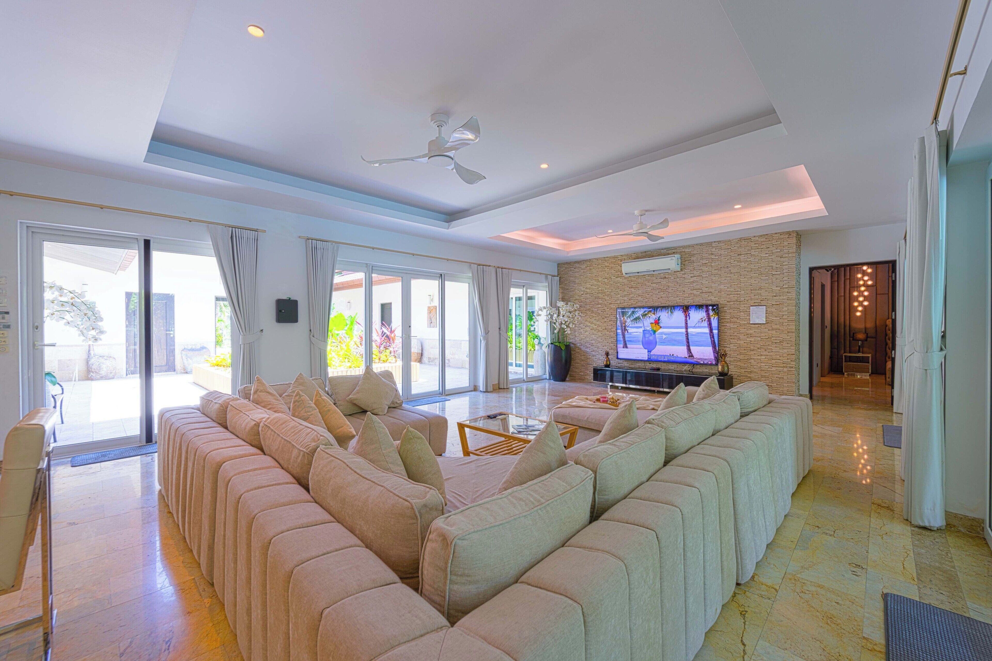 A spacious living room with a large sectional sofa, a flat-screen TV, and a ceiling fan.