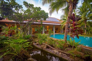 A pool surrounded by tropical plants and a building with a tiled roof. - 6BR Luxury Tropical Pool Villa PH125 (Cha-am)