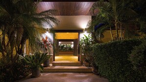 A well-lit entrance with a stone pathway leading to a wooden door, surrounded by lush tropical plants. - 6BR Luxury Tropical Pool Villa PH125 (Cha-am)