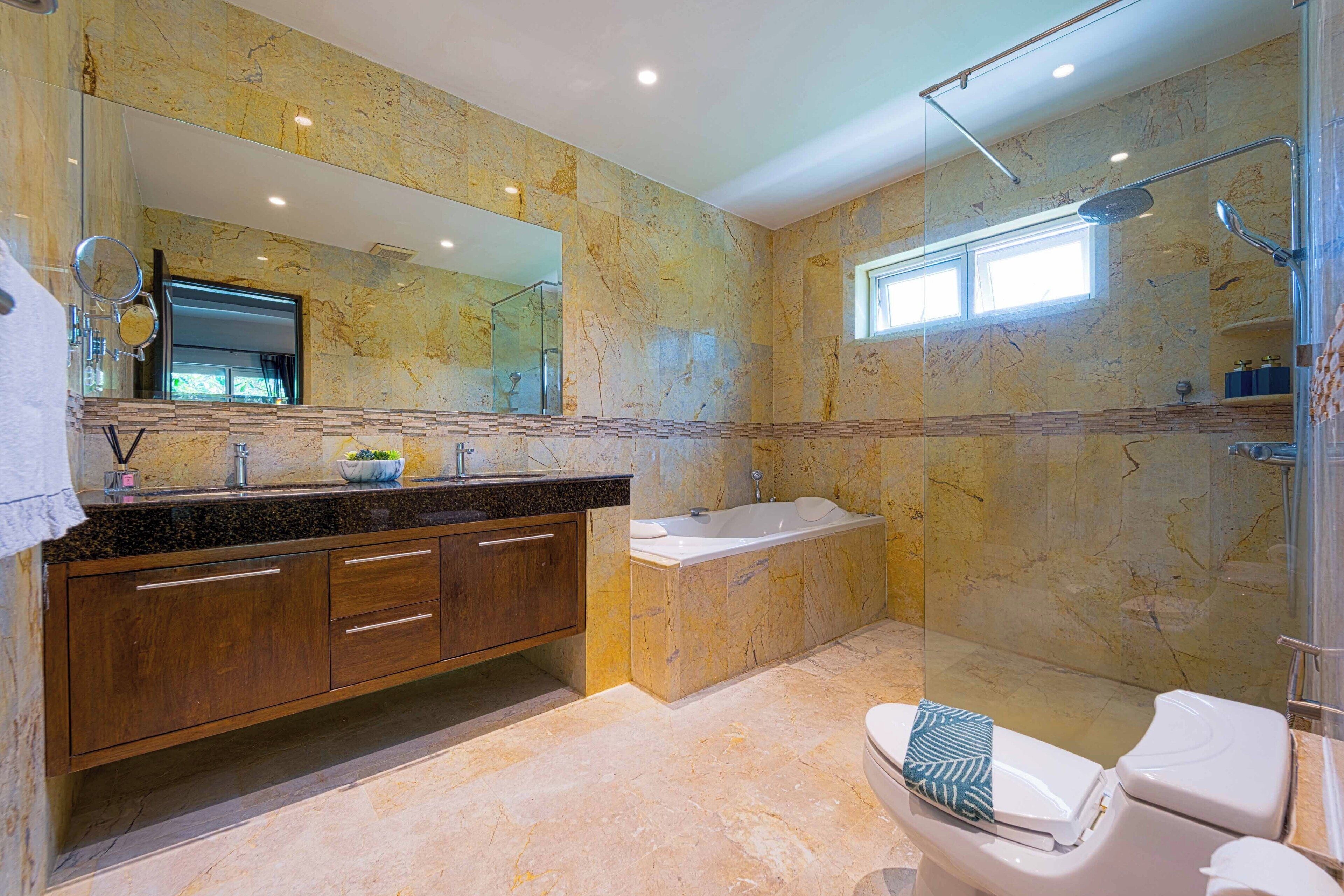 A modern bathroom with a marble wall, a large mirror, a bathtub, and a toilet.