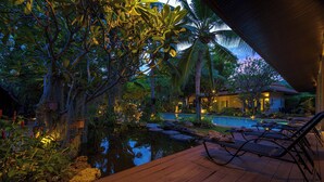 A serene pool area with lounge chairs, a wooden deck, and lush tropical vegetation. - 6BR Luxury Tropical Pool Villa PH125 (Cha-am)