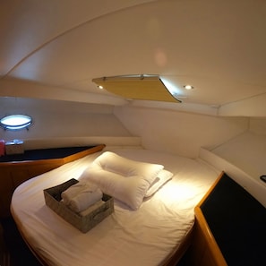 A compact, well-lit cabin with a single bed, a small seating area, and a built-in shelf. - Yacht King (Busan)
