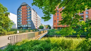 A modern apartment building with balconies, a pedestrian bridge, and lush greenery.