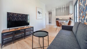 A modern living room with a flat-screen TV, a sofa, a small table, and a dining area in the background.