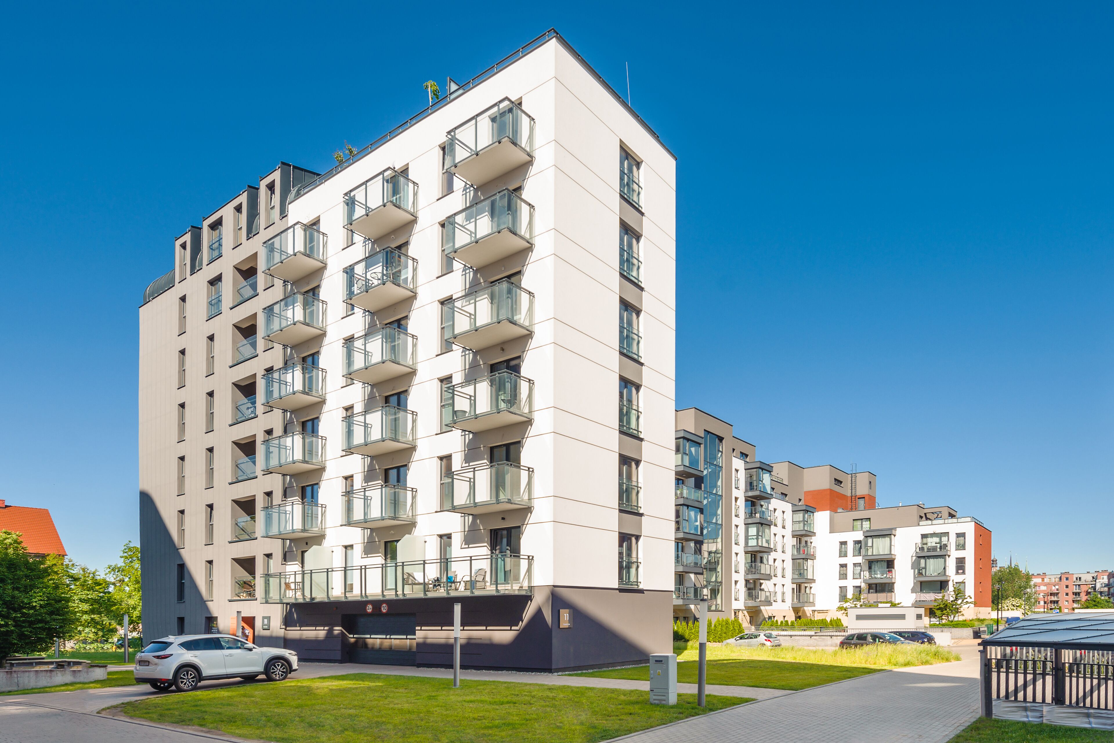 Een modern meerlaags woongebouw met balkons, een parkeerplaats en een verzorgd gazon.