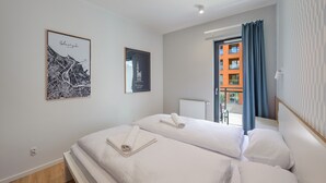 A hotel room with two beds, a cityscape artwork, a framed picture, and a view of a building through a window.