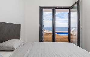 A bedroom with a bed, a view of the sea through a sliding glass door, and a wooden deck with chairs. - Lovely home in Kosljun (Kosljun)